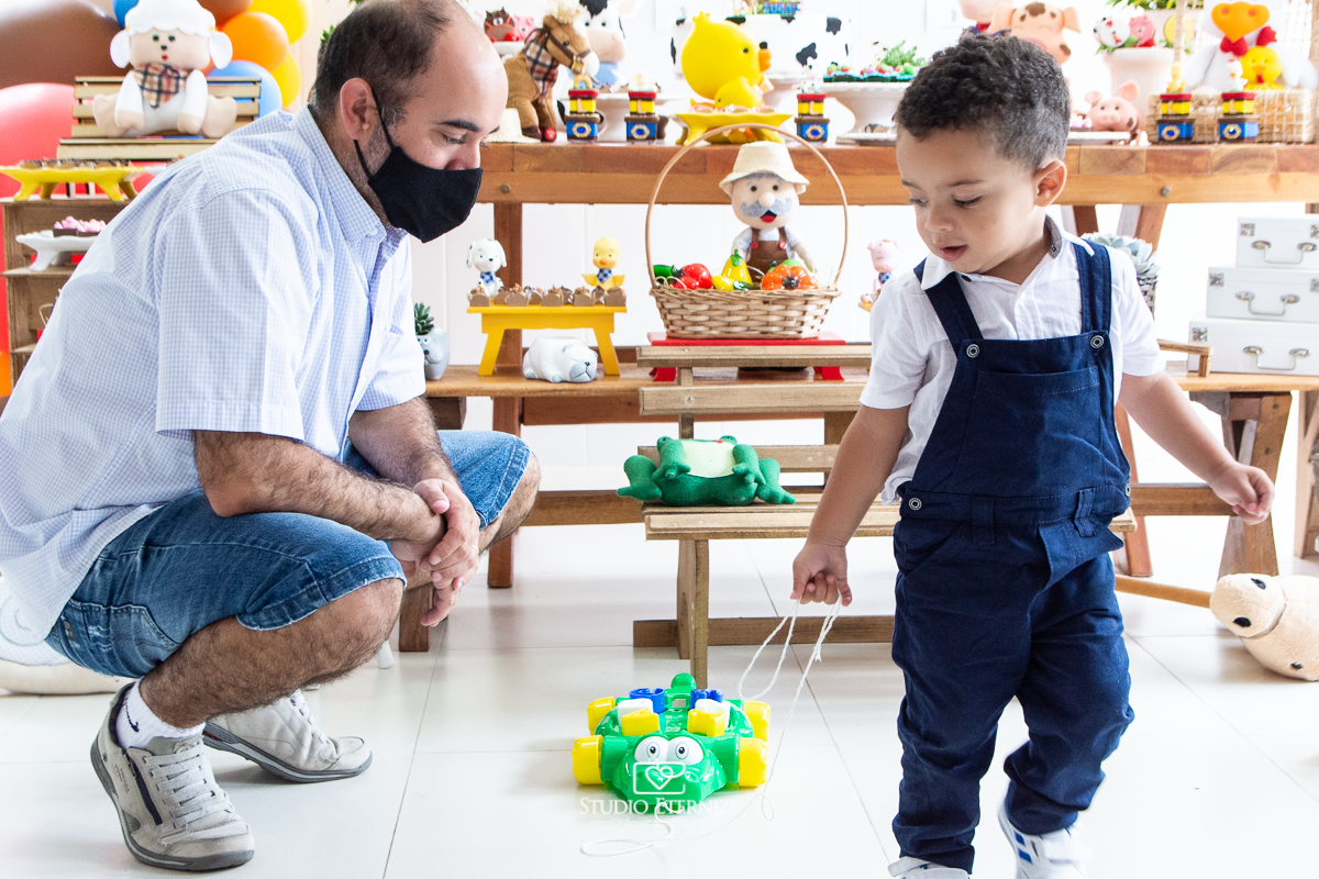 Fotografia de festa infantil de 2 anos registrada pelo Studio Eternize no tema da fazendinha em Poços de Caldas - MG. Aniversariante brinca com presente que ganhou, um carrinho em formato de jacaré, puxando sua cordinha.