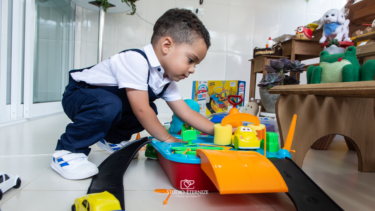 Fotografia de festa infantil de 2 anos registrada pelo Studio Eternize no tema da fazendinha em Poços de Caldas - MG. Aniversariante brinca com presente que ganhou, uma pista de carrinhos.