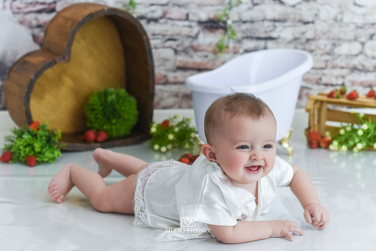 Fotografia de acompanhamento mensal do bebê realizada no Studio Eternize em Poços de Caldas - MG. Bebê menina com 6 meses de idade vestida de roupão de cetim de bruços.