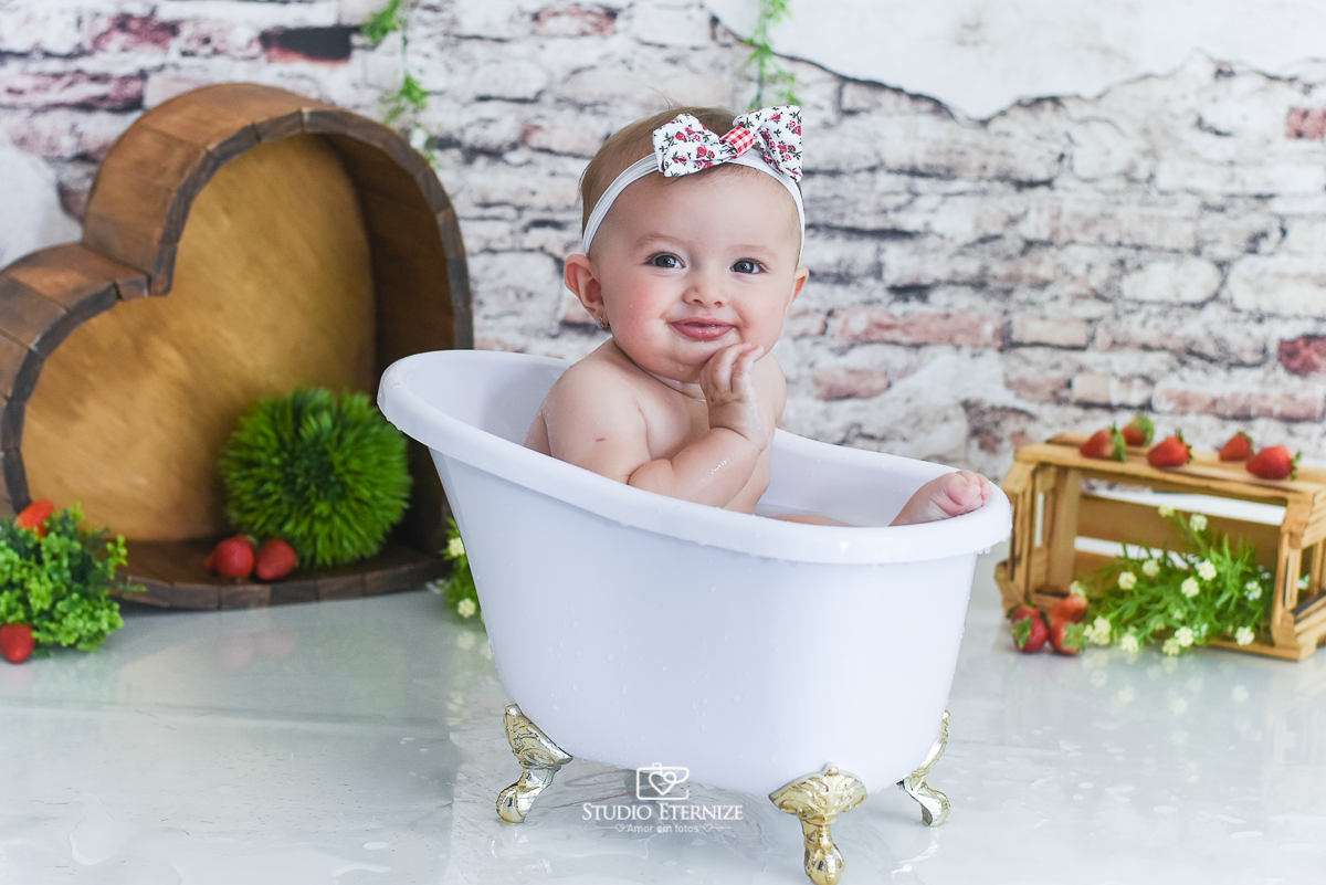 Fotografia de acompanhamento mensal do bebê realizada no Studio Eternize em Poços de Caldas - MG. Bebê menina com 6 meses de idade dentro de uma banheira branca e as pontas dos dedos do pé para fora.