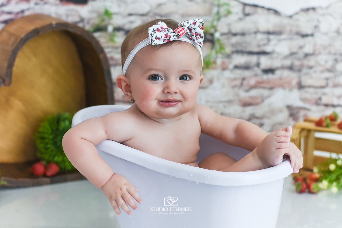 Fotografia de acompanhamento mensal do bebê realizada no Studio Eternize em Poços de Caldas - MG. Bebê menina com 6 meses de idade dentro de uma banheira branca e um dos pés para fora.