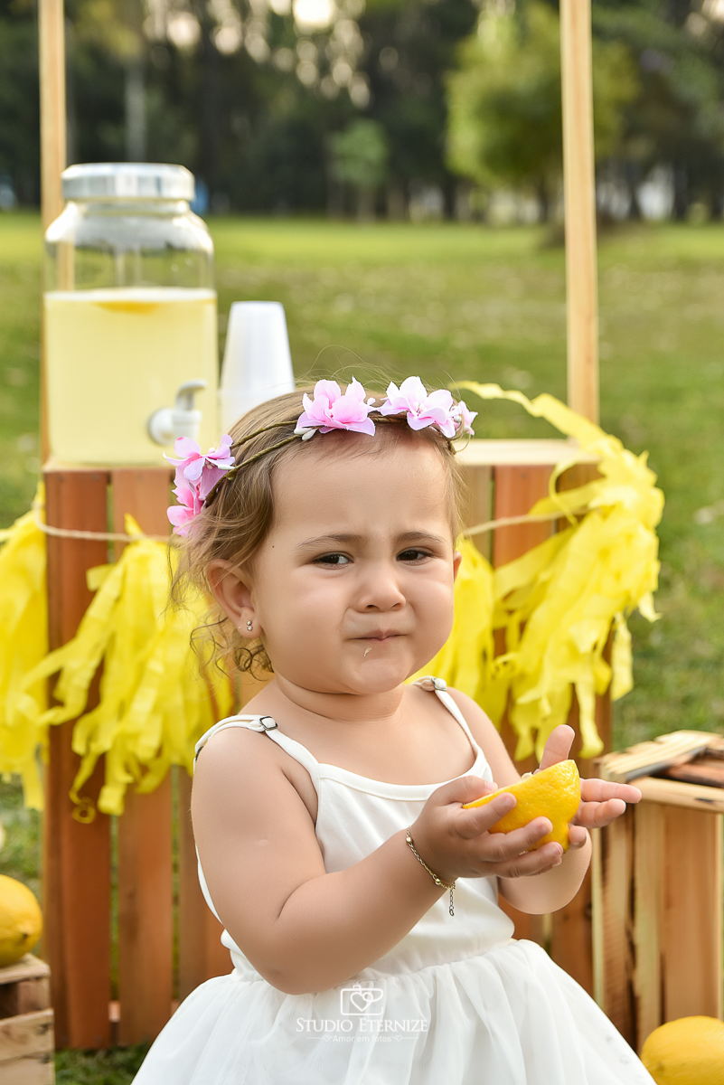Sessão fotográfica infantil externa com cenário da barraca da limonada. Close da careta da criança que experimentou um limão siciliano.