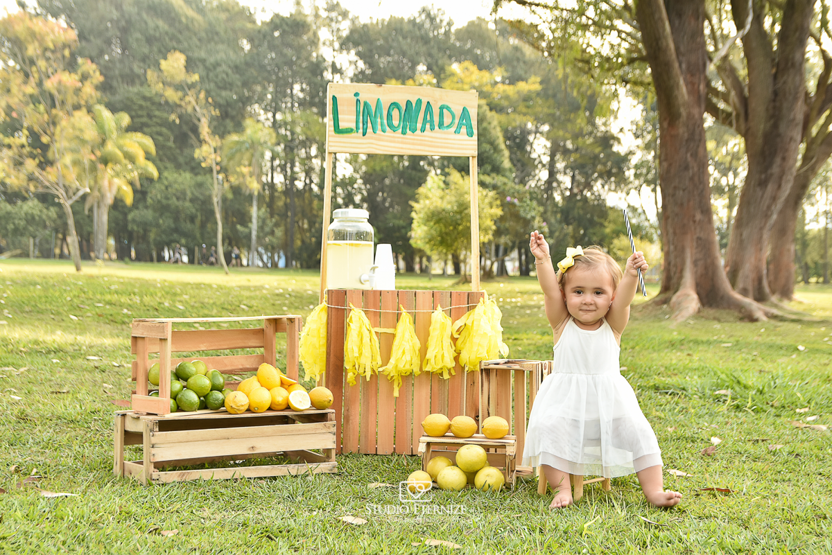 Sessão fotográfica infantil externa com cenário da barraca da limonada. A criança estava levantando os braços, comemorando.