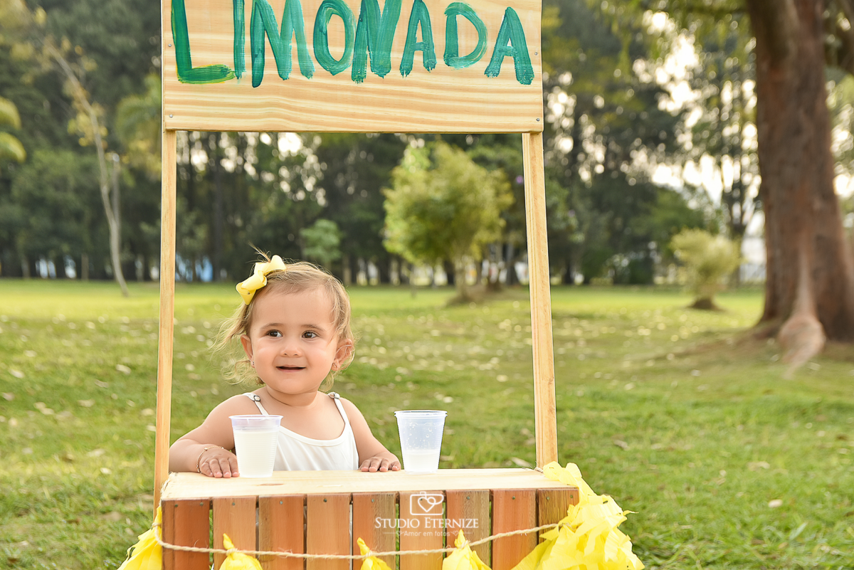 Sessão fotográfica infantil externa com cenário da barraca da limonada. Close da criança que estava atrás da barraca da limonada sorrindo.