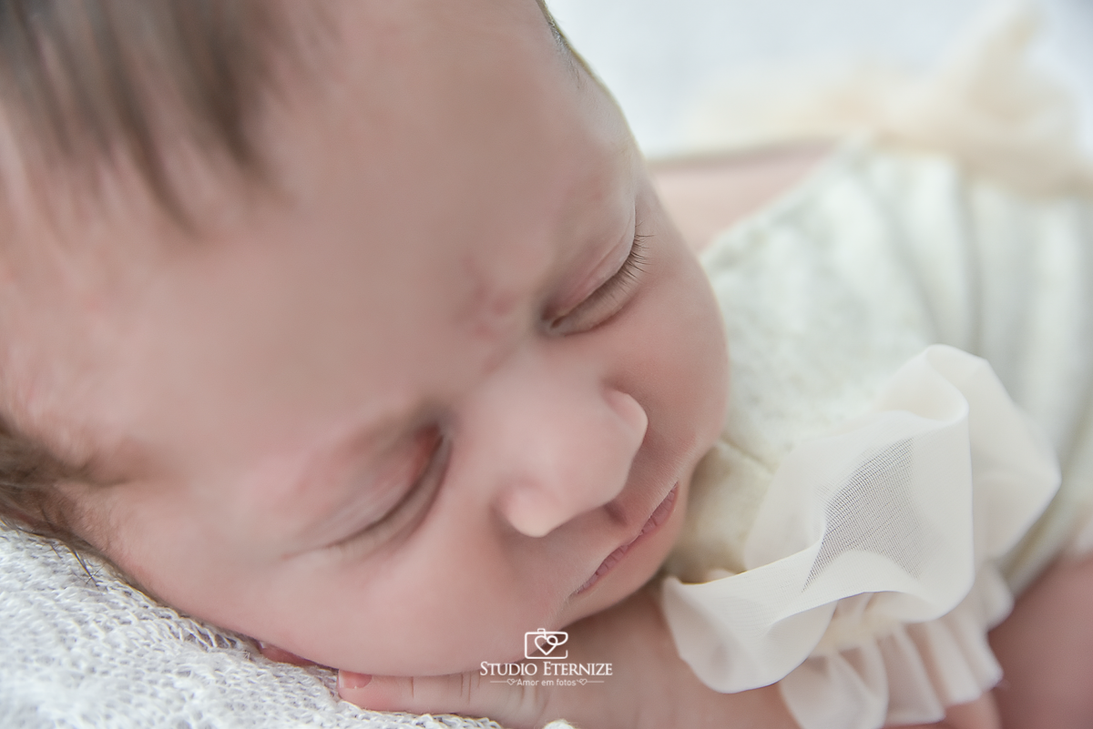 Fotografia newborn menina realizada pelo Studio Eternize em Poços de Caldas - MG. Detalhe do rostinho da bebê na pose de bundinha no puff com uma manta branca.