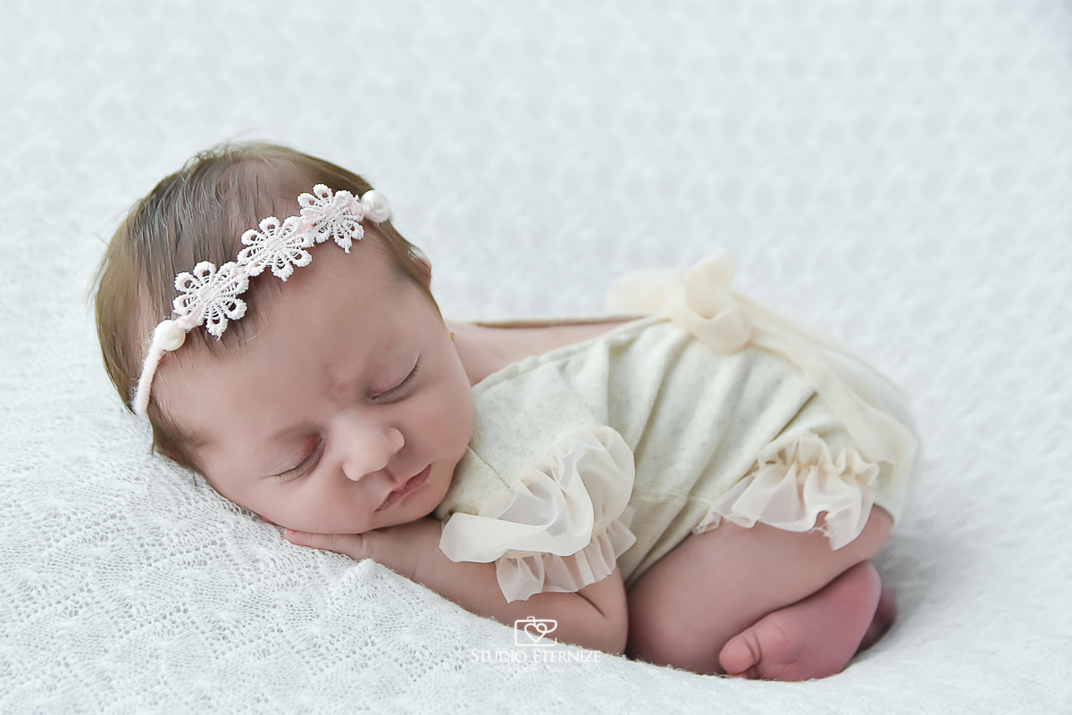 Fotografia newborn menina realizada pelo Studio Eternize em Poços de Caldas - MG. Bebê na pose de bundinha no puff com uma manta branca.