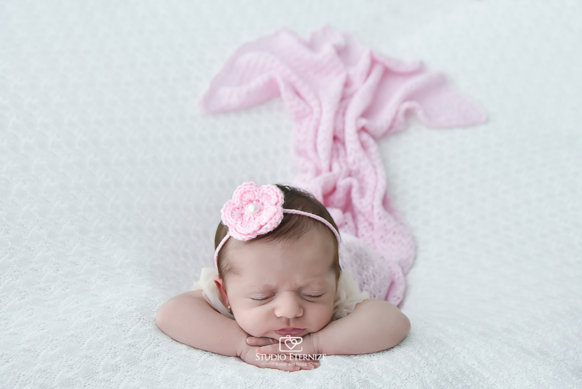 Fotografia newborn menina realizada pelo Studio Eternize em Poços de Caldas - MG. Bebê na pose de bracinho de frente no puff com uma manta branca. Tecido rosa atrás da bebê imitando uma cauda de sereia.