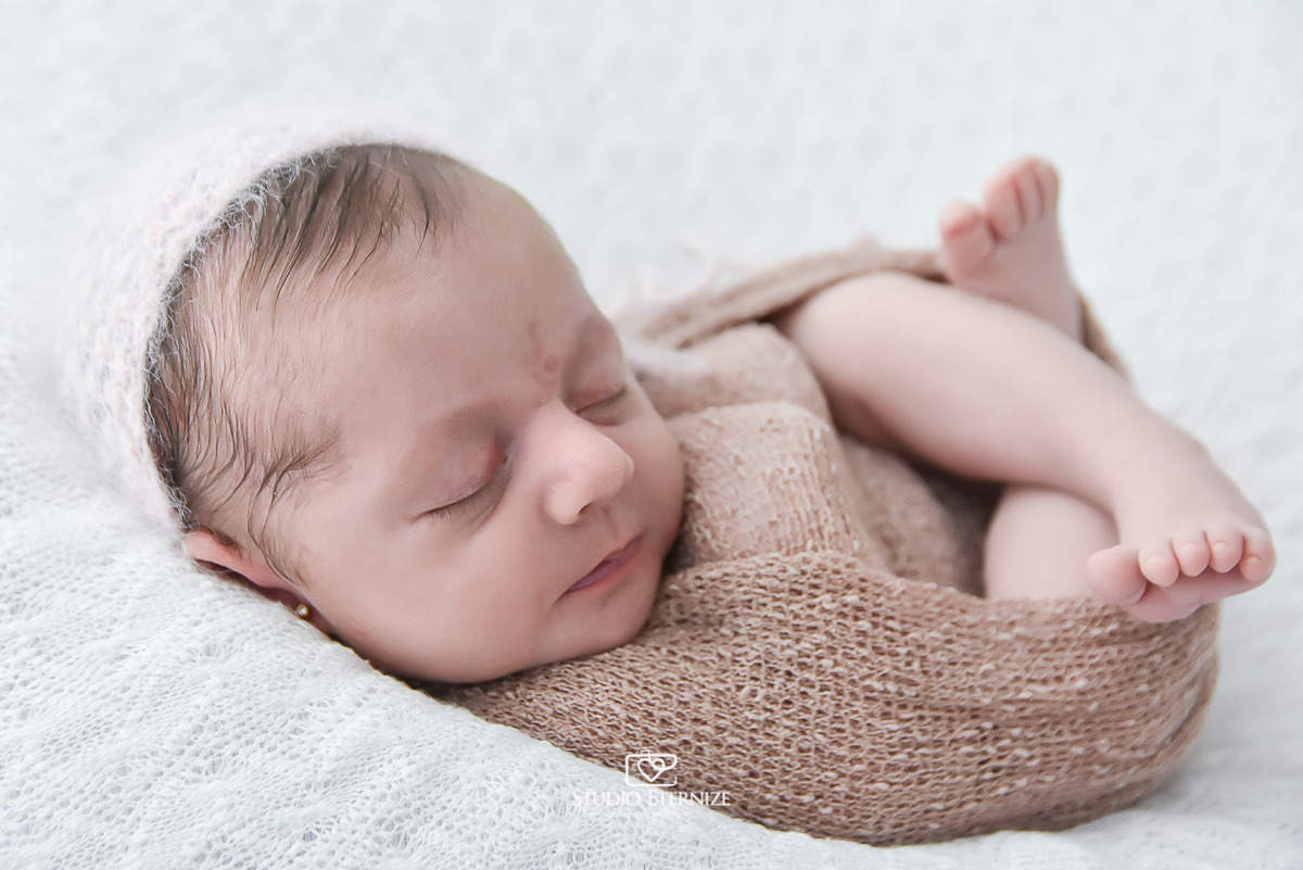Fotografia newborn menina realizada pelo Studio Eternize em Poços de Caldas - MG. Bebê enroladinha no wrap de barriguinha para cima, no puff com uma manta branca.