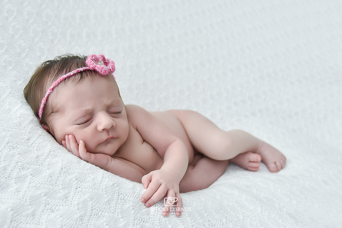 Fotografia newborn menina realizada pelo Studio Eternize em Poços de Caldas - MG. Bebê na pose de ladinho no puff com uma manta branca.