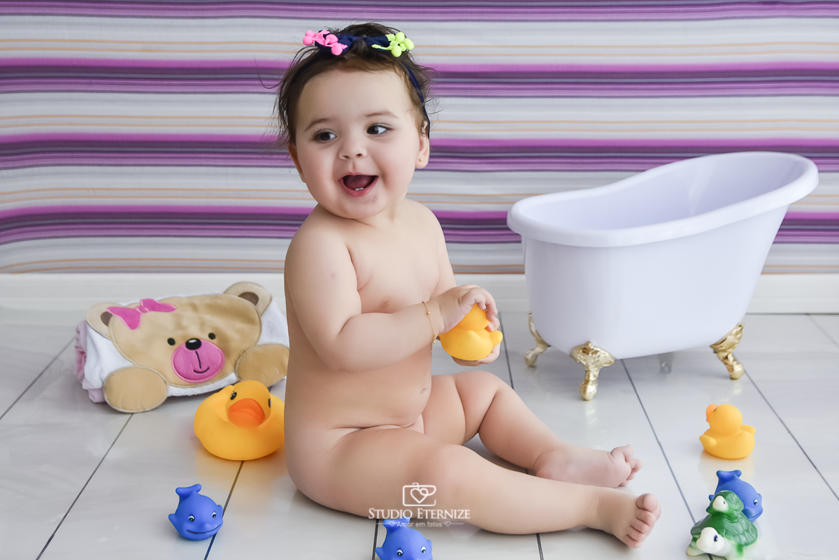 Fotografia de acompanhamento mensal do bebê. Menina. 8 meses. Ensaio de banho. Peladinha brincando com os patinhos de borracha.