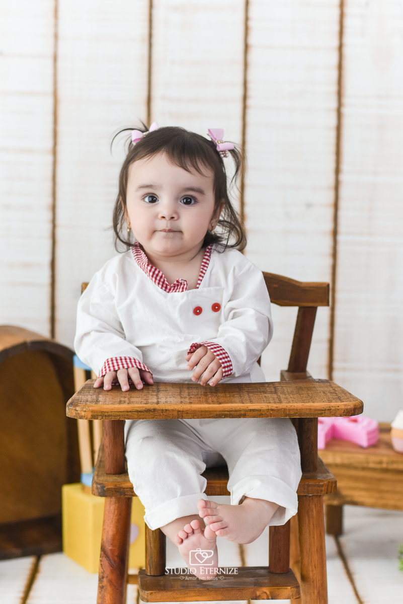 Fotografia de acompanhamento mensal do bebê realizada no Studio Eternize em Poços de Caldas - MG. Bebê menina com 9 meses de idade, tema da sessão de cozinheiro. Close dela vestida de cozinheira, sentada no cadeirão.