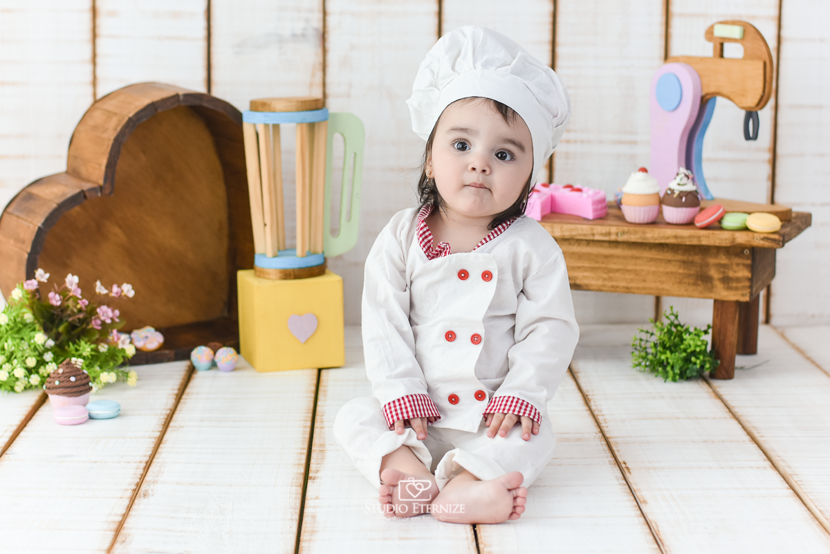 Fotografia de acompanhamento mensal do bebê realizada no Studio Eternize em Poços de Caldas - MG. Bebê menina com 9 meses de idade, tema da sessão de cozinheiro. Ela está vestida de cozinheira, sentada no cenário.