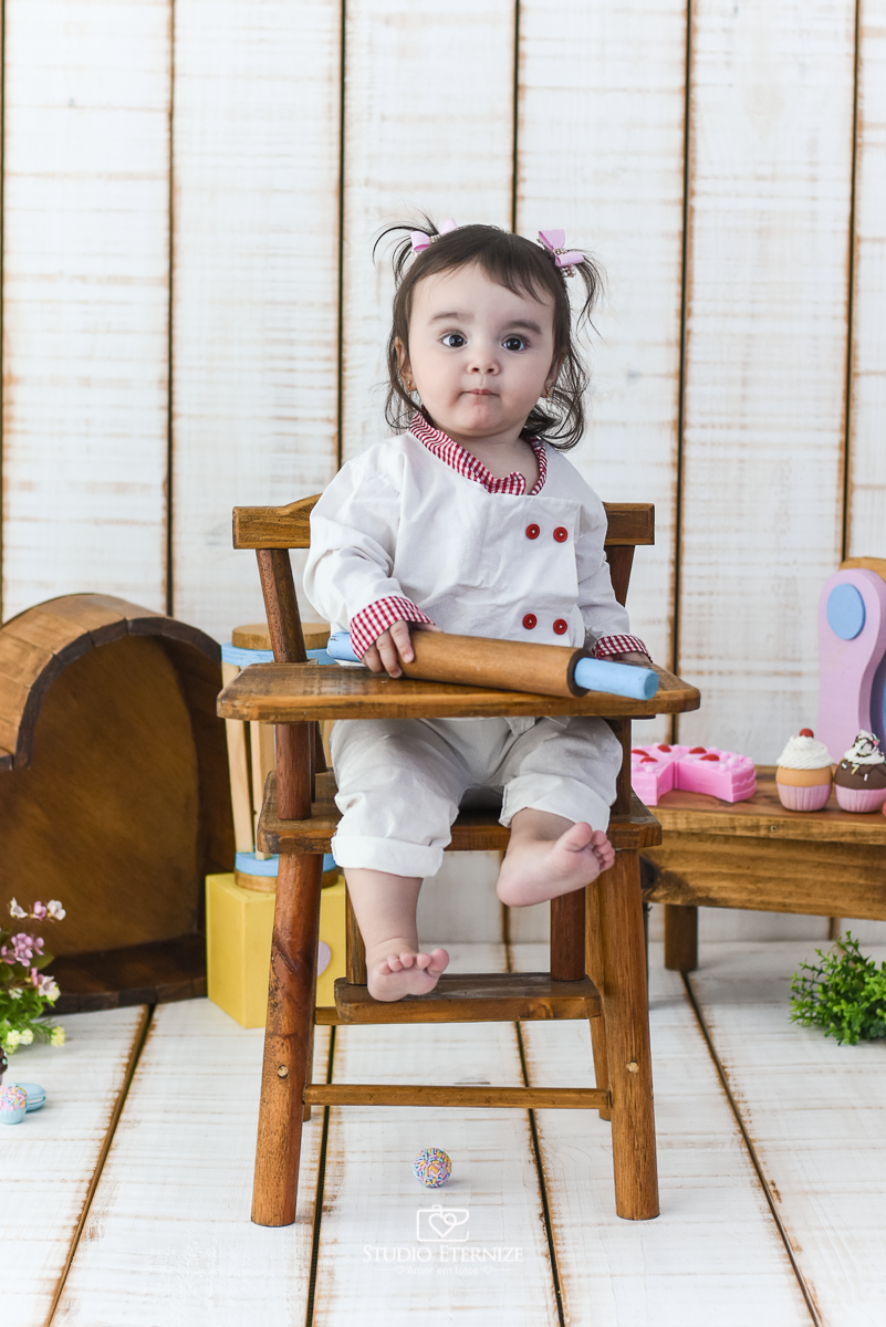 Fotografia de acompanhamento mensal do bebê realizada no Studio Eternize em Poços de Caldas - MG. Bebê menina com 9 meses de idade, tema da sessão de cozinheiro. Ela está vestida de cozinheira, sentada no cadeirão.