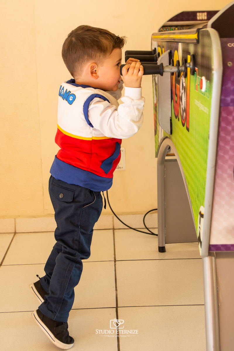 Fotografia de festa infantil de 3 anos registrada pelo Studio Eternize no tema da Patrulha Canina em no Buffet Cata-Vento em Poços de Caldas - MG. Aniversariante brincando na mesa de pebolim.