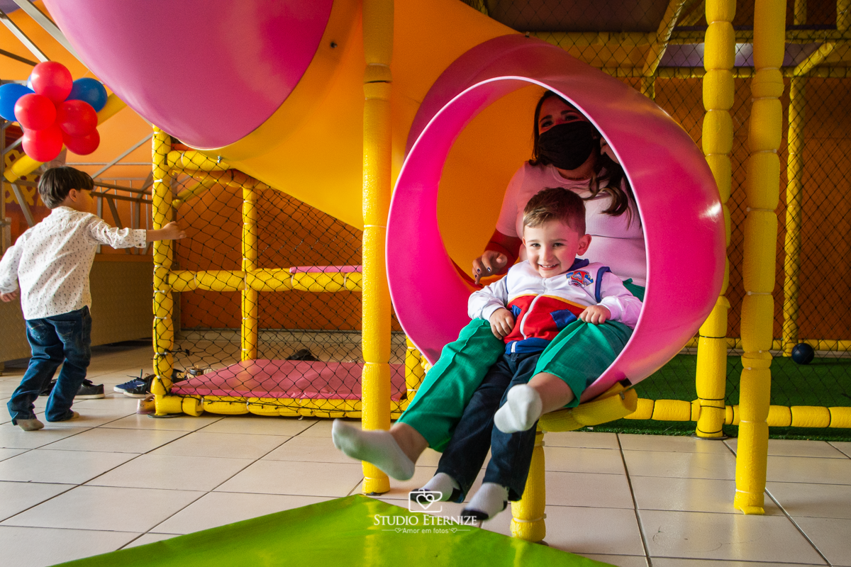 Fotografia de festa infantil de 3 anos registrada pelo Studio Eternize no tema da Patrulha Canina em no Buffet Cata-Vento em Poços de Caldas - MG. Aniversariante brincando no escorrega com sua mãe.