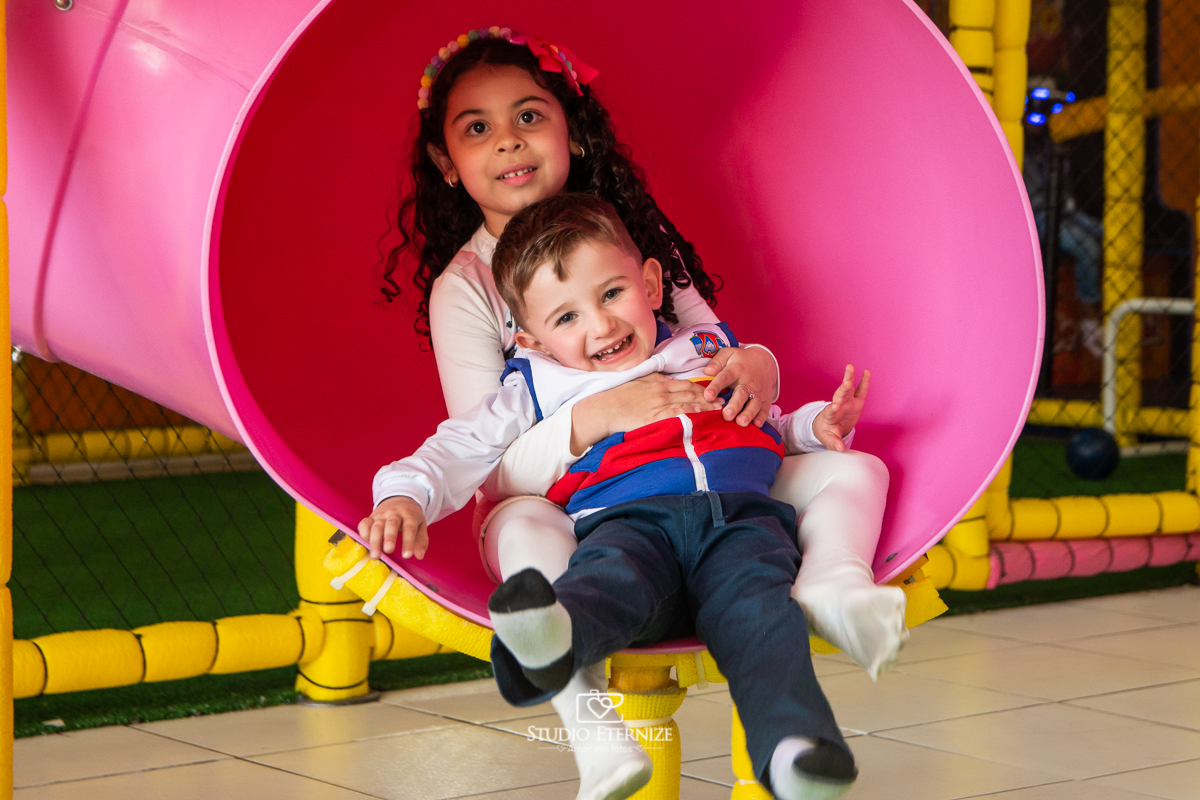 Fotografia de festa infantil de 3 anos registrada pelo Studio Eternize no tema da Patrulha Canina em no Buffet Cata-Vento em Poços de Caldas - MG. Aniversariante brincando no escorrega com sua prima.