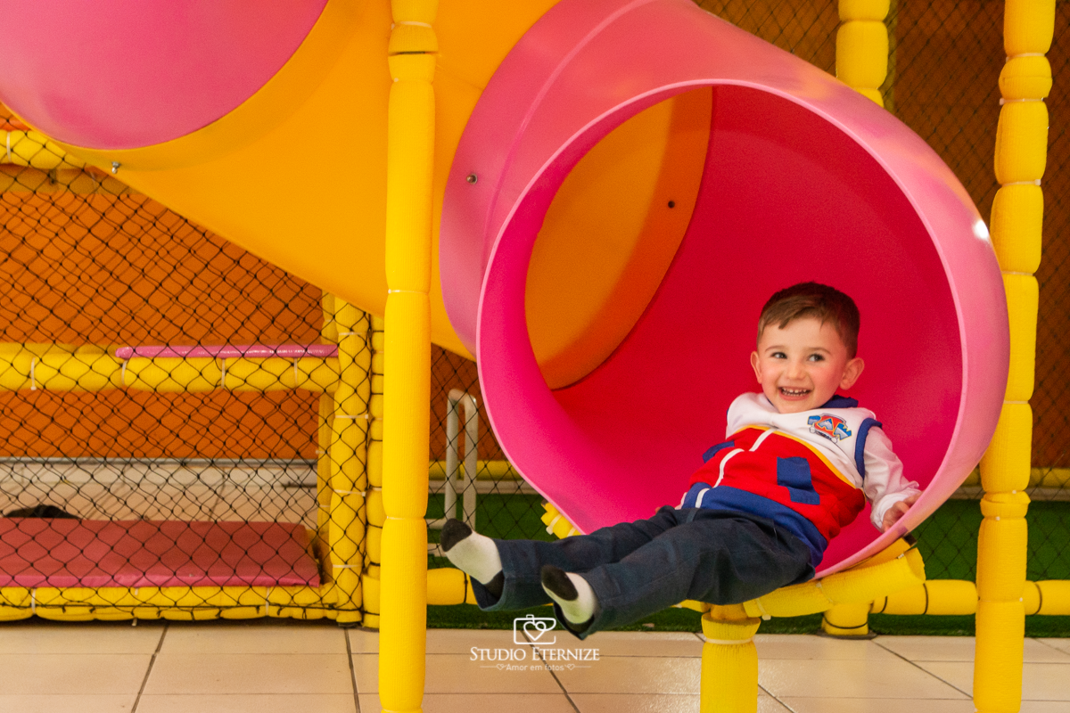 Fotografia de festa infantil de 3 anos registrada pelo Studio Eternize no tema da Patrulha Canina em no Buffet Cata-Vento em Poços de Caldas - MG. Aniversariante brincando no escorrega.