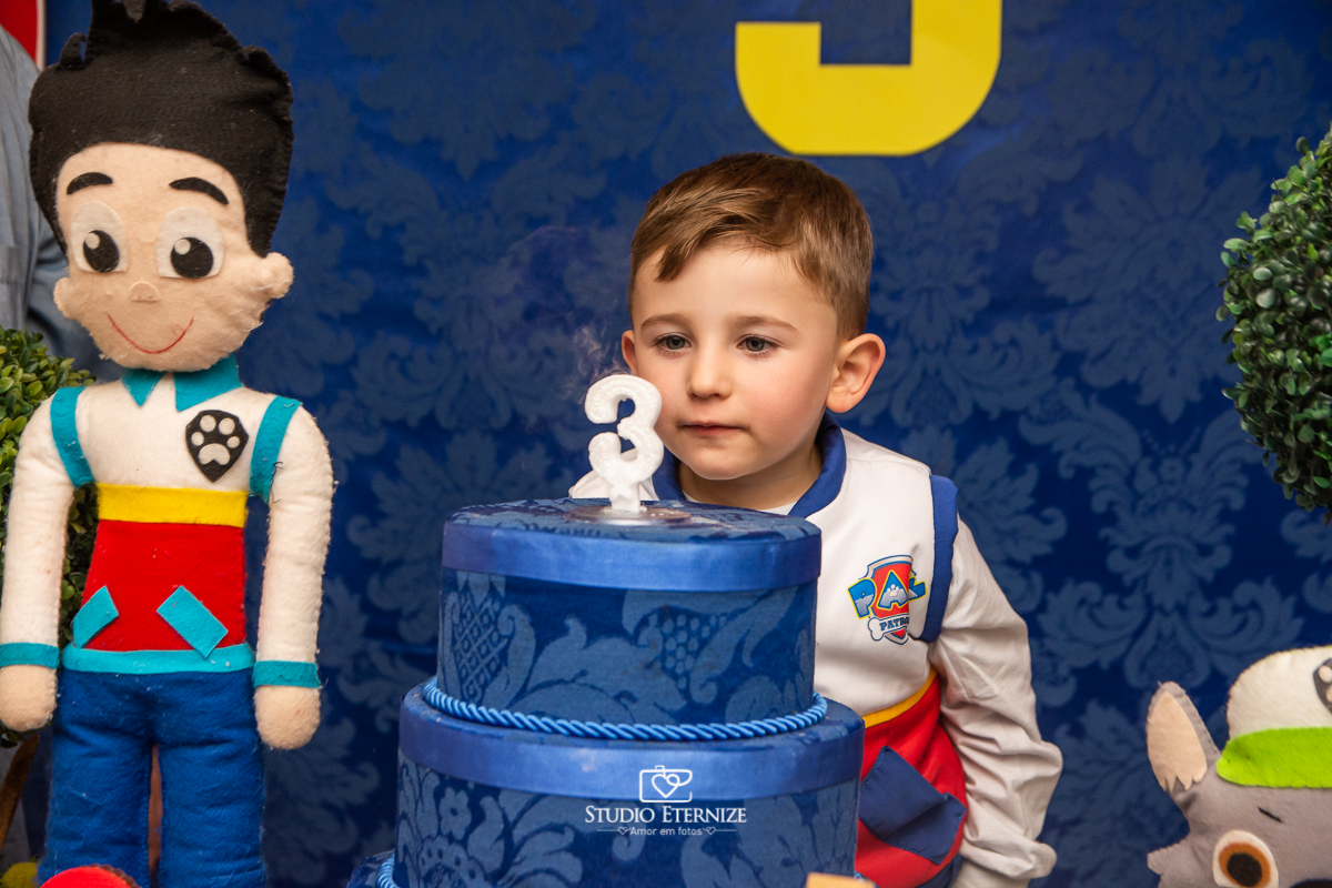 Fotografia de festa infantil de 3 anos registrada pelo Studio Eternize no tema da Patrulha Canina em no Buffet Cata-Vento em Poços de Caldas - MG. Aniversariante soprando a vela do bolo.