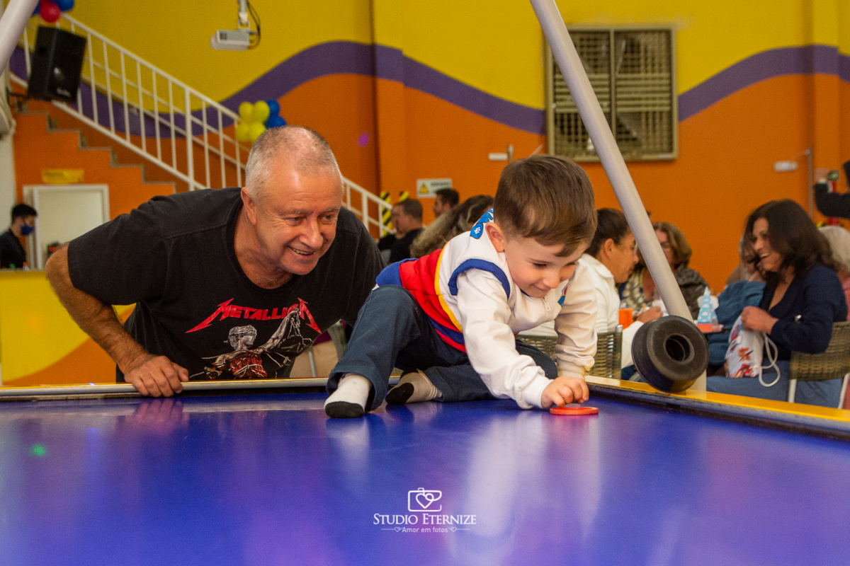 Fotografia de festa infantil de 3 anos registrada pelo Studio Eternize no tema da Patrulha Canina em no Buffet Cata-Vento em Poços de Caldas - MG. Aniversariante brincando na mesa de futebol com seu avô.