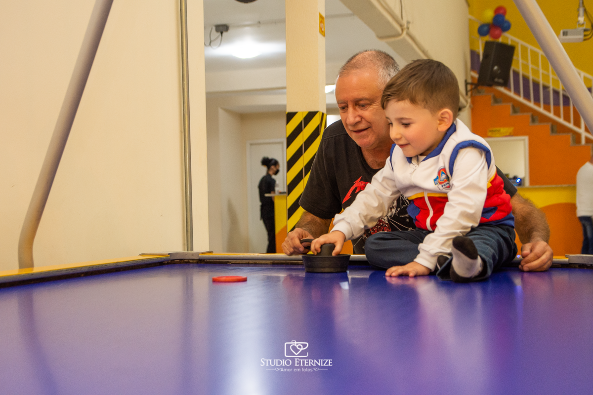 Fotografia de festa infantil de 3 anos registrada pelo Studio Eternize no tema da Patrulha Canina em no Buffet Cata-Vento em Poços de Caldas - MG. Aniversariante brincando na mesa de futebol com seu avô.