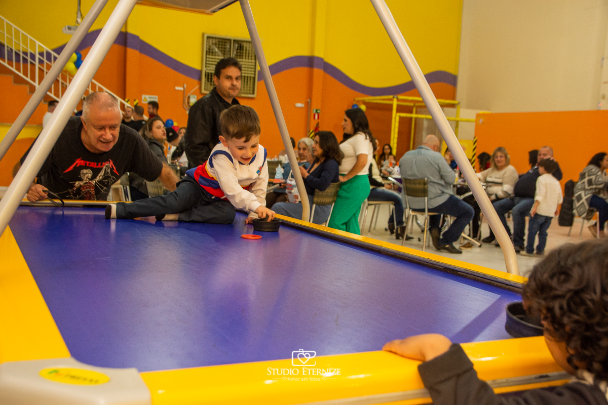 Fotografia de festa infantil de 3 anos registrada pelo Studio Eternize no tema da Patrulha Canina em no Buffet Cata-Vento em Poços de Caldas - MG. Aniversariante brincando na mesa de futebol com seu avô.
