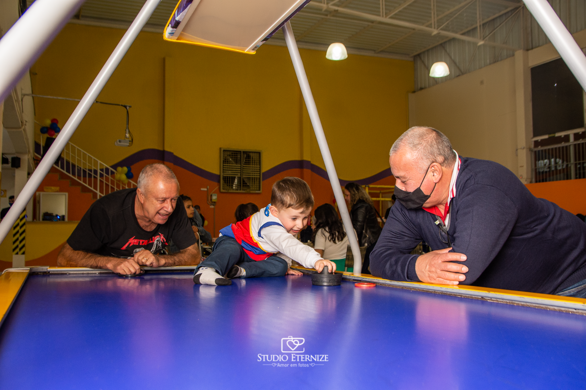 Fotografia de festa infantil de 3 anos registrada pelo Studio Eternize no tema da Patrulha Canina em no Buffet Cata-Vento em Poços de Caldas - MG. Aniversariante brincando na mesa de futebol com seu avô.