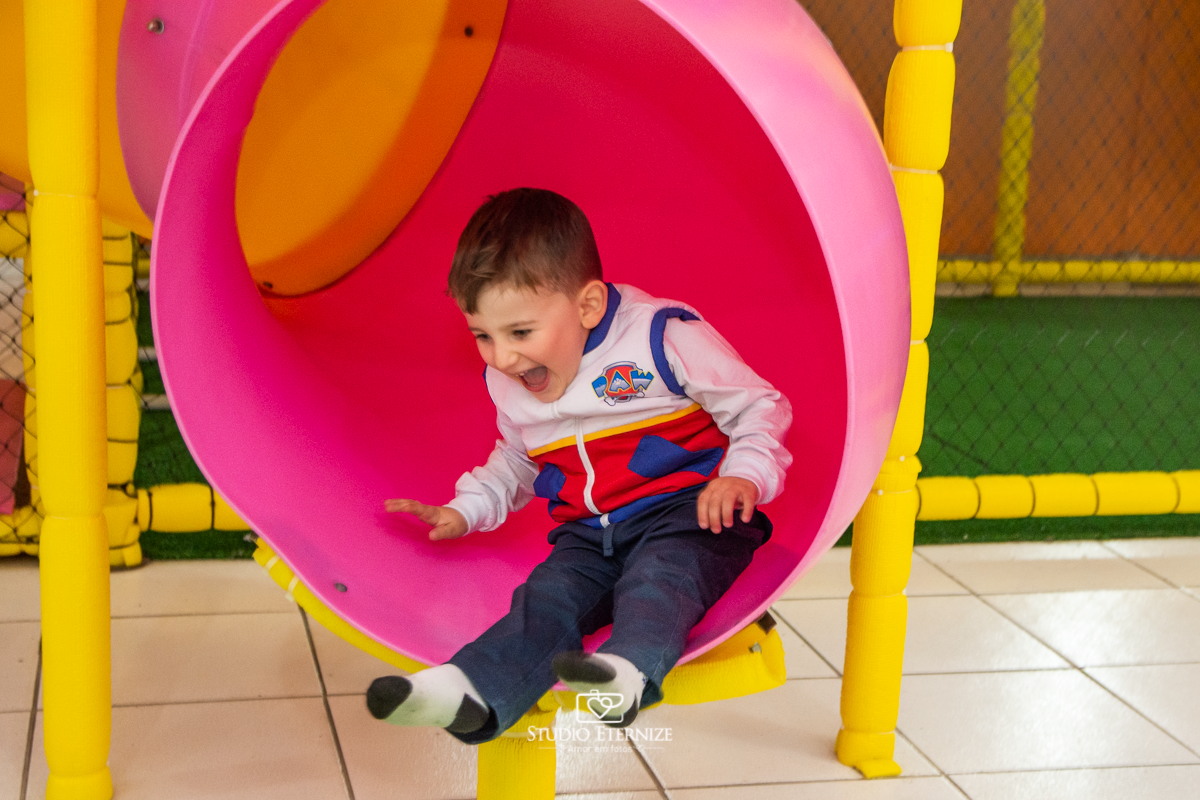 Fotografia de festa infantil de 3 anos registrada pelo Studio Eternize no tema da Patrulha Canina em no Buffet Cata-Vento em Poços de Caldas - MG. Aniversariante brincando no escorrega.