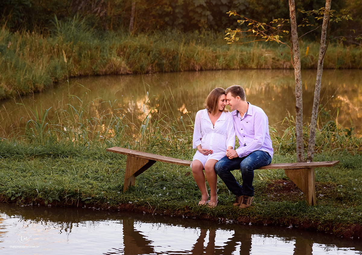 casal de grávidos sentado no banco na beira do lago em um dia de sol e vento agradável