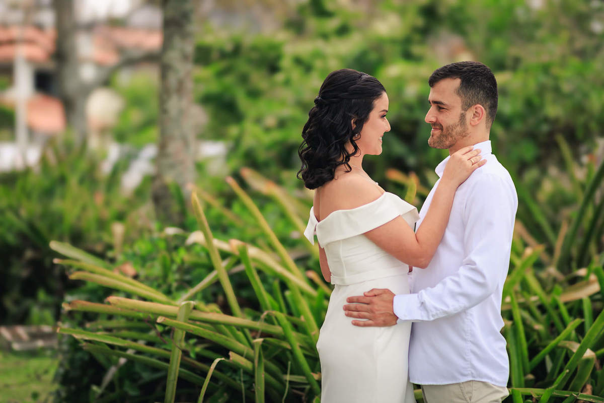 Djonata e Aline trocando olhares apaixonados em um cenário romântico à beira-mar em Coqueiros, Florianópolis.
