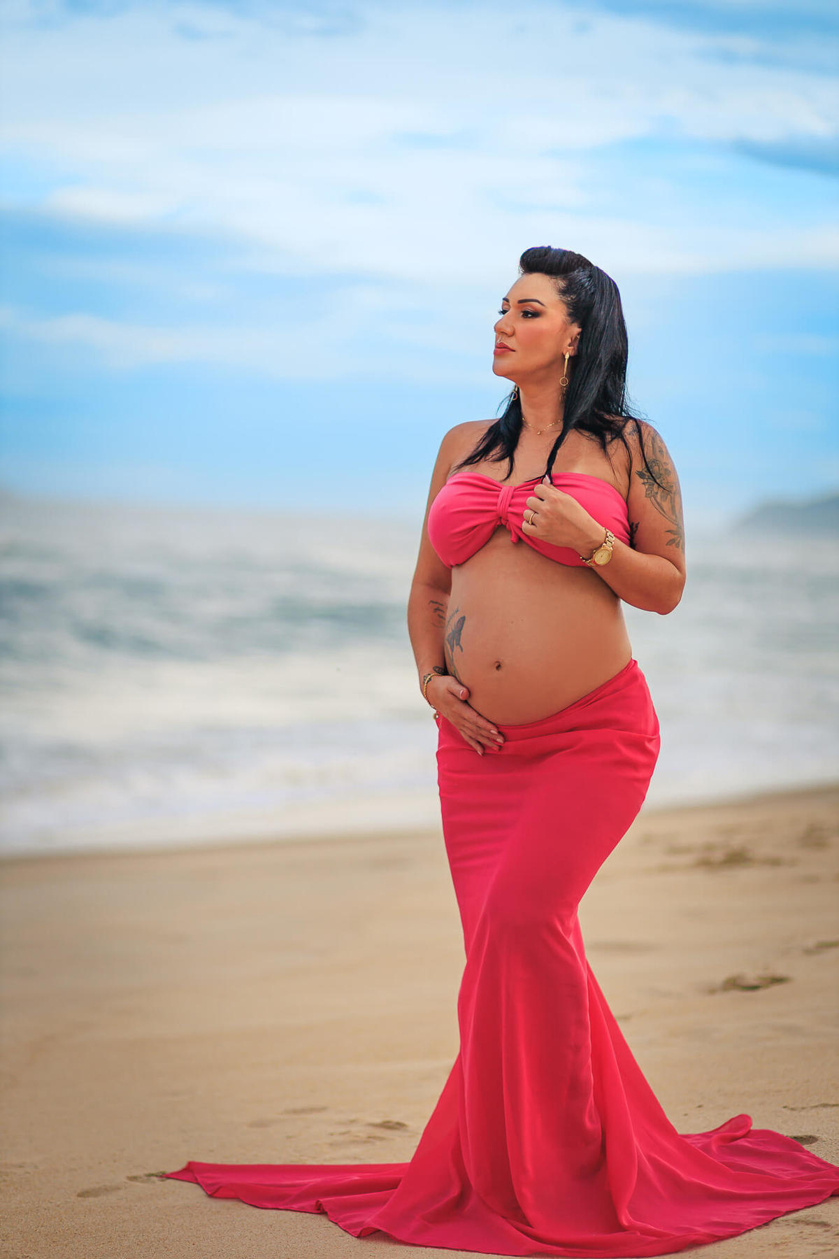 Foto de casal caminhando de mãos dadas pela areia em um ensaio gestante na praia.