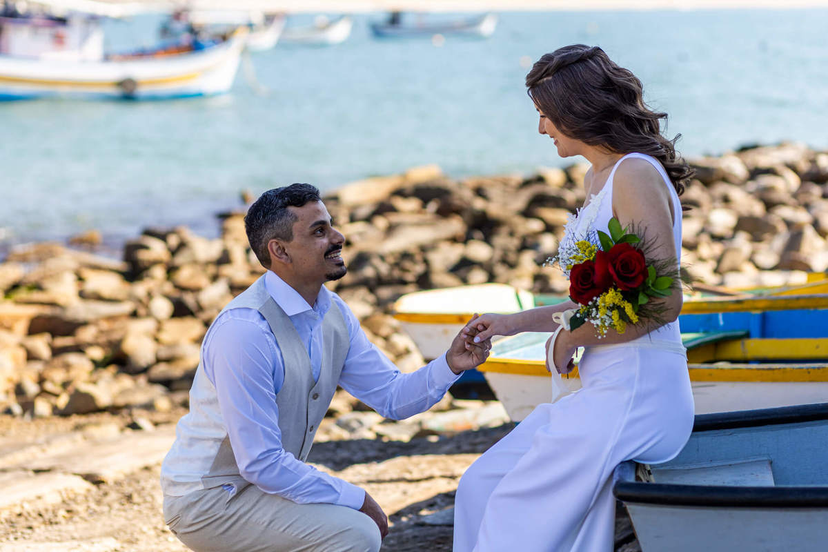 Noivos abraçados e sentados em um banco no píer da Praia da Armação, em um ensaio de fotografia de casal.