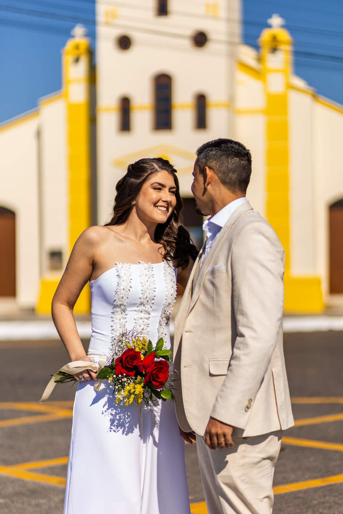 Casal de noivos sorrindo em frente à igreja amarela da Praia da Armação, no Sul da Ilha, Florianópolis.