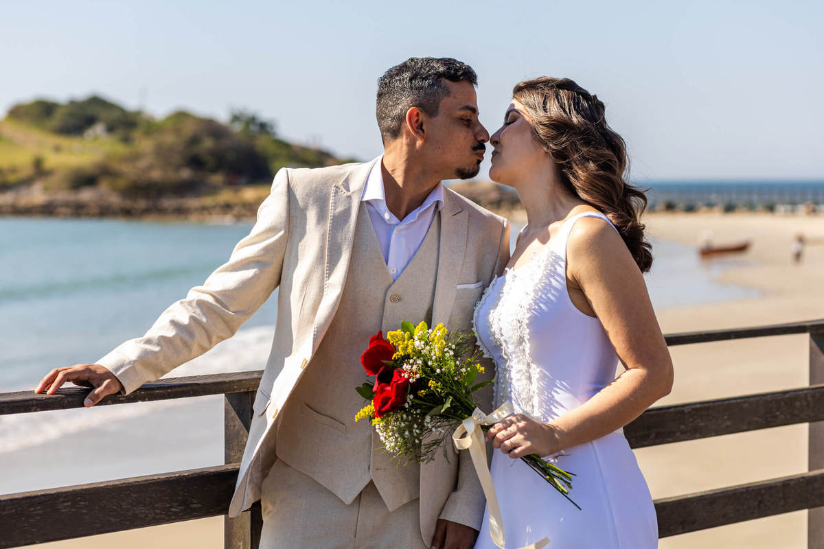 Casal de noivos se beijando no píer da Praia da Armação durante ensaio de casamento em Florianópolis.
