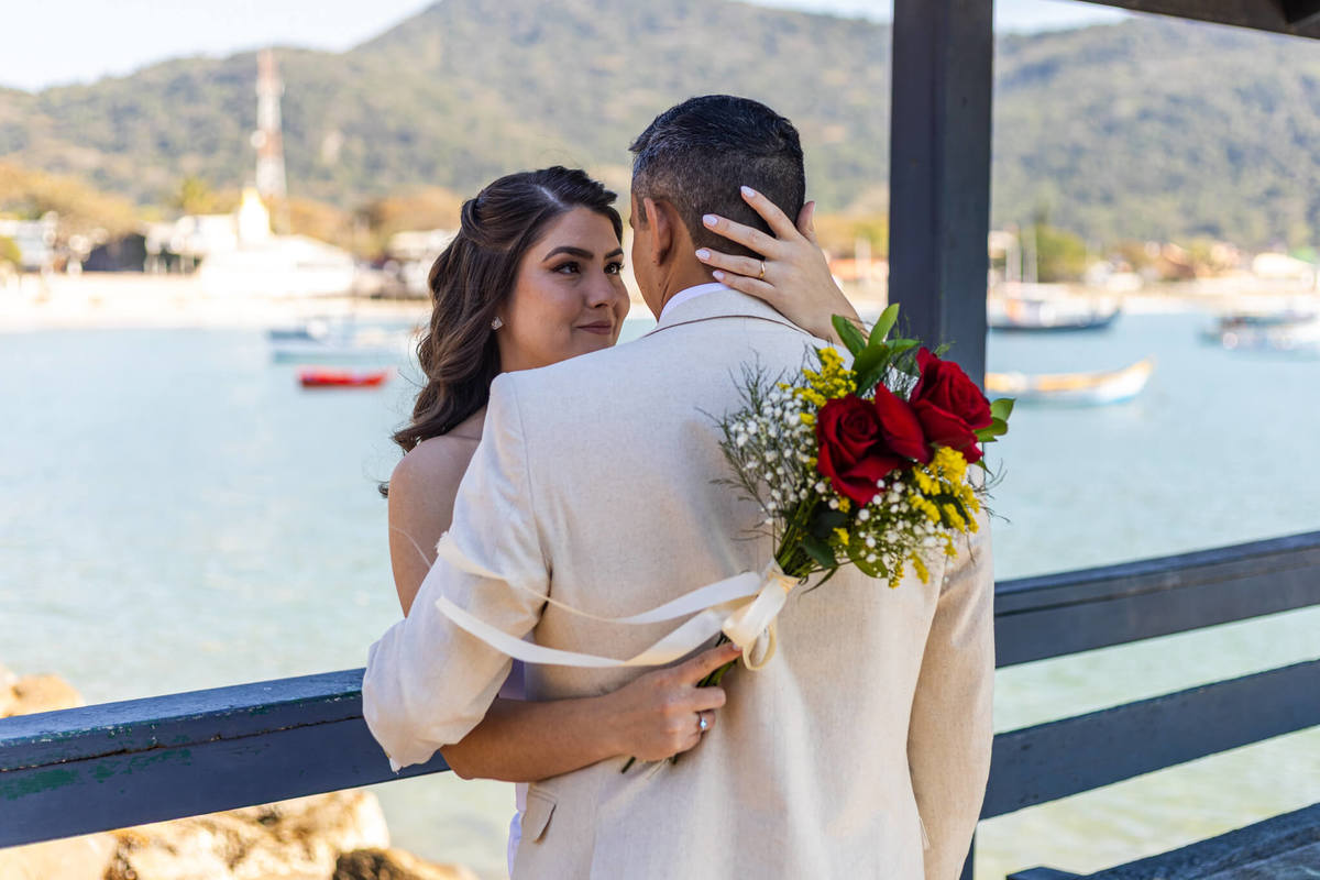 Noivos em um momento romântico no píer da Praia da Armação, ensaio fotográfico em Florianópolis.