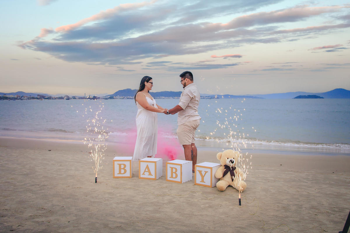Família caminhando de mãos dadas na areia durante o chá revelação na praia em Florianópolis, ao pôr do sol.