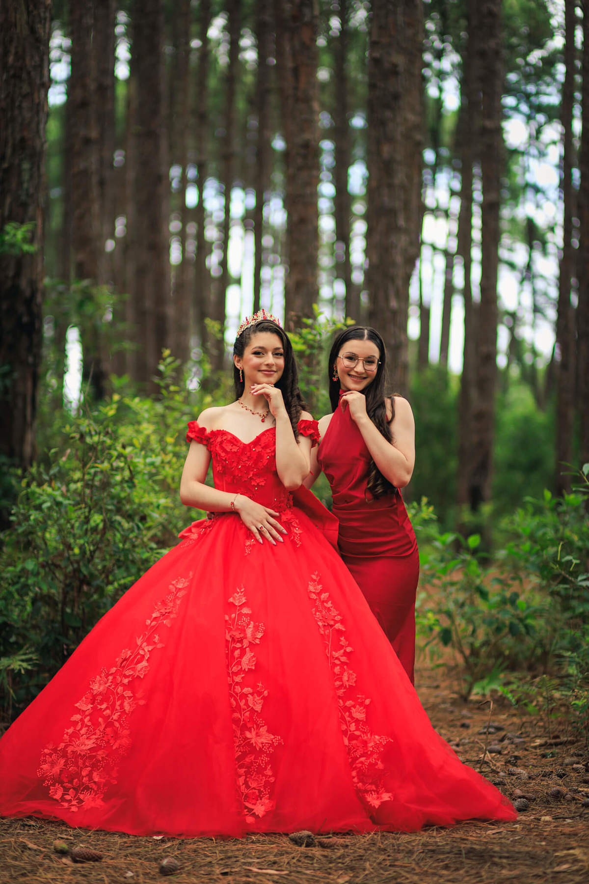 Legna posando sorridente ao lado de convidada, ambas vestindo vermelho, em meio às árvores do Bosque do Moçambique em Florianópolis.
