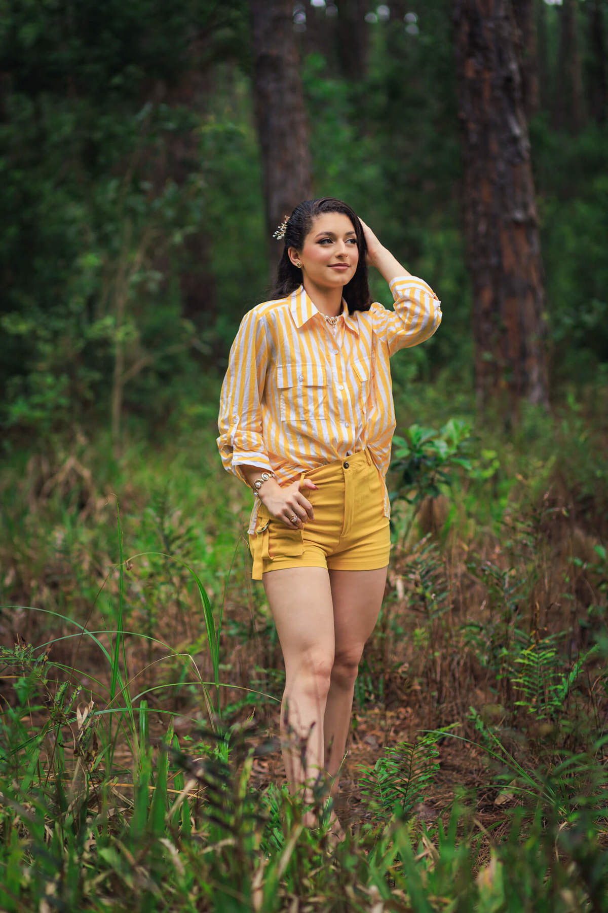 Debutante posando em pé sobre um tronco de árvore caído no meio da floresta, demonstrando atitude e estilo jovem.
