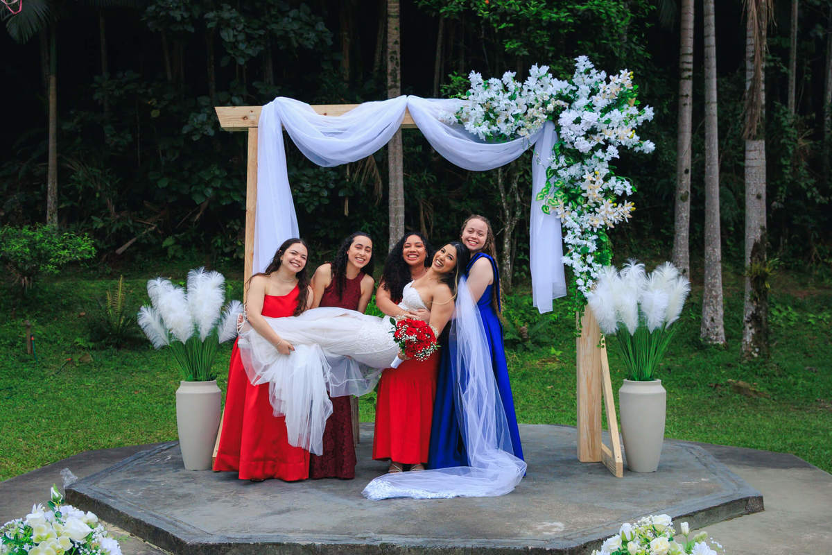 Noiva Harluine sendo carregada pelas madrinhas durante casamento ao ar livre.