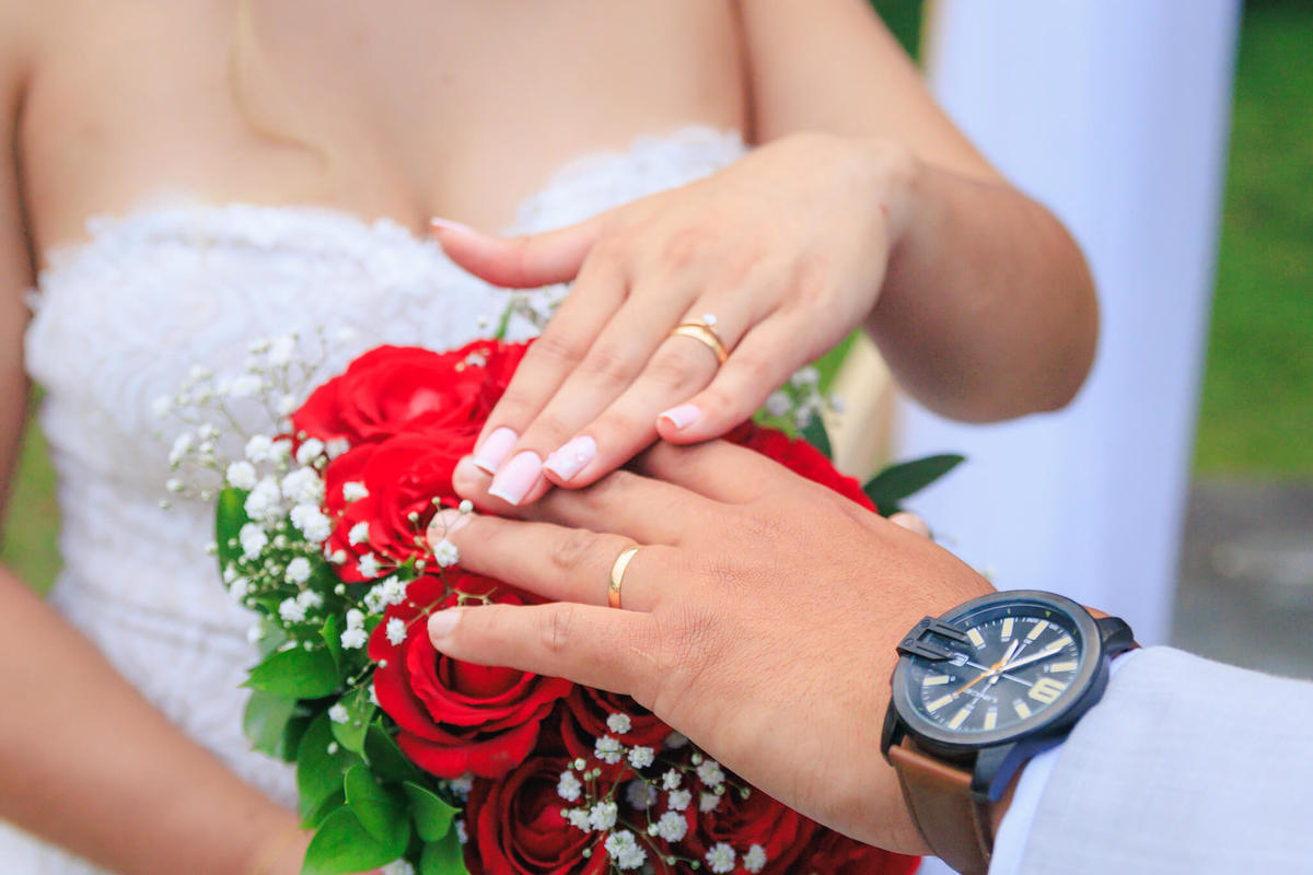 Detalhe das alianças dos noivos sobre o buquê de rosas vermelhas.