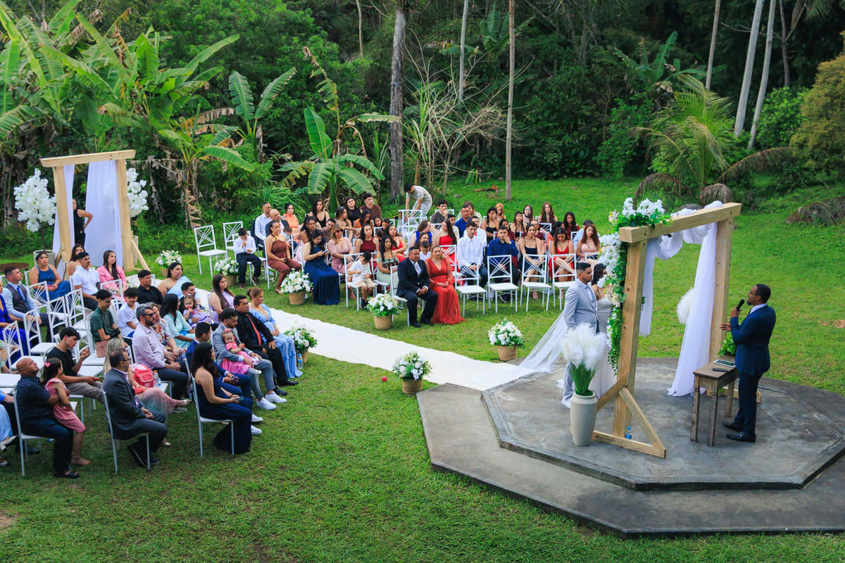 Vista ampla da cerimônia de casamento ao ar livre com convidados e decoração floral.