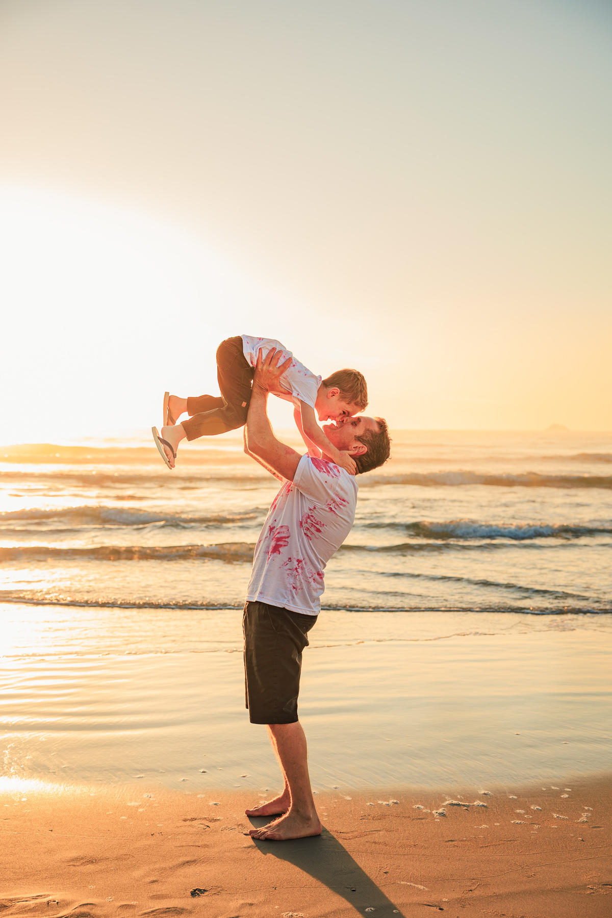 Pai levantando o filho durante ensaio de família ao pôr do sol.