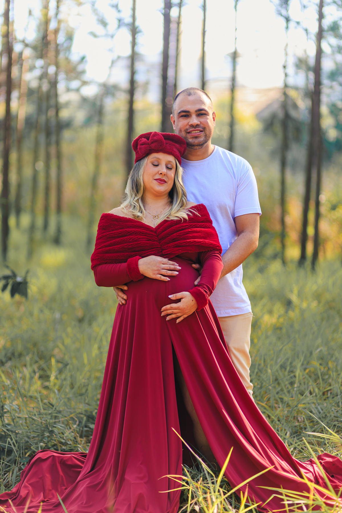 Casal abraçado durante ensaio de gestante com vestido vermelho em
área de mata.