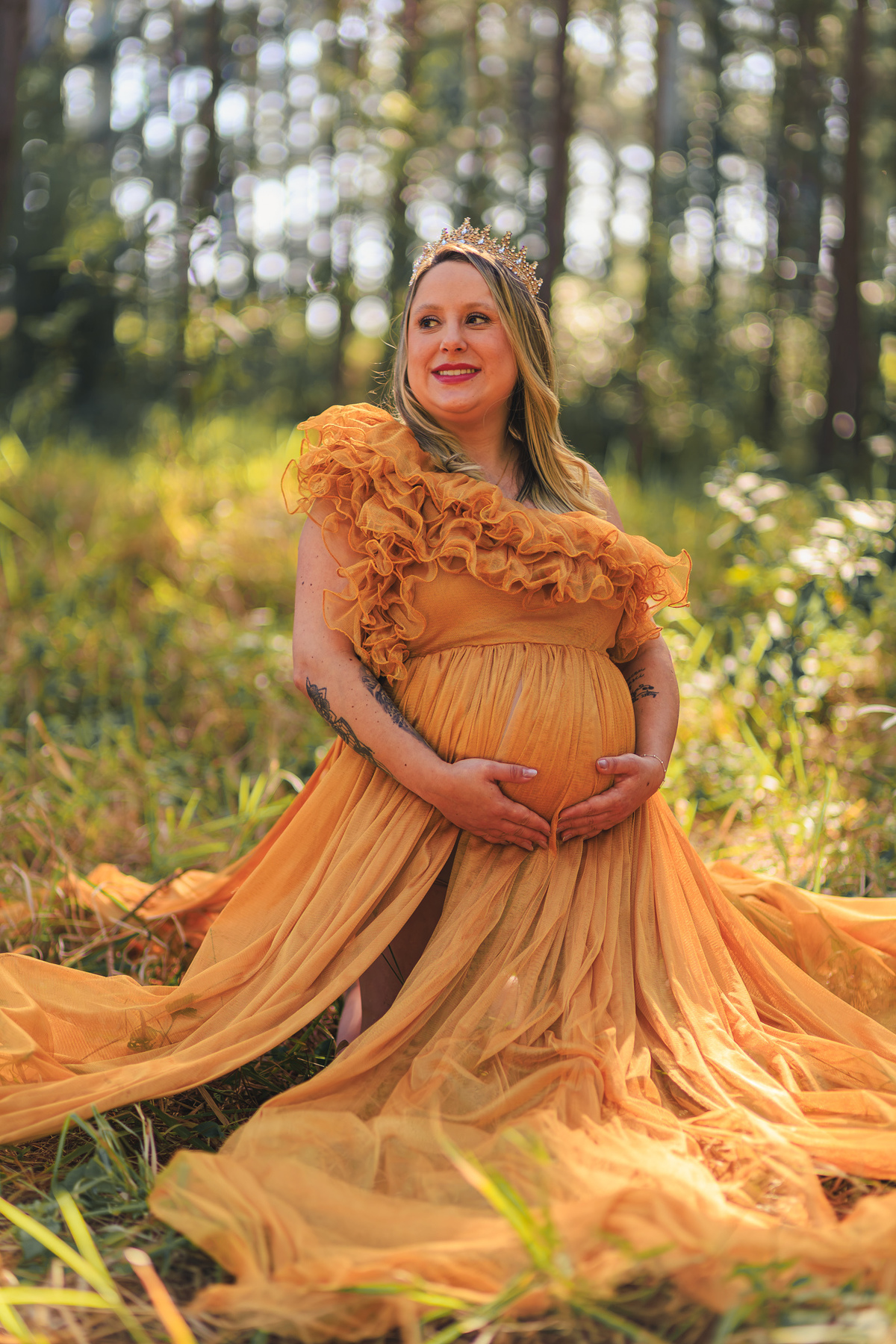 Retrato de Thais grávida com vestido dourado e coroa em meio à
natureza.