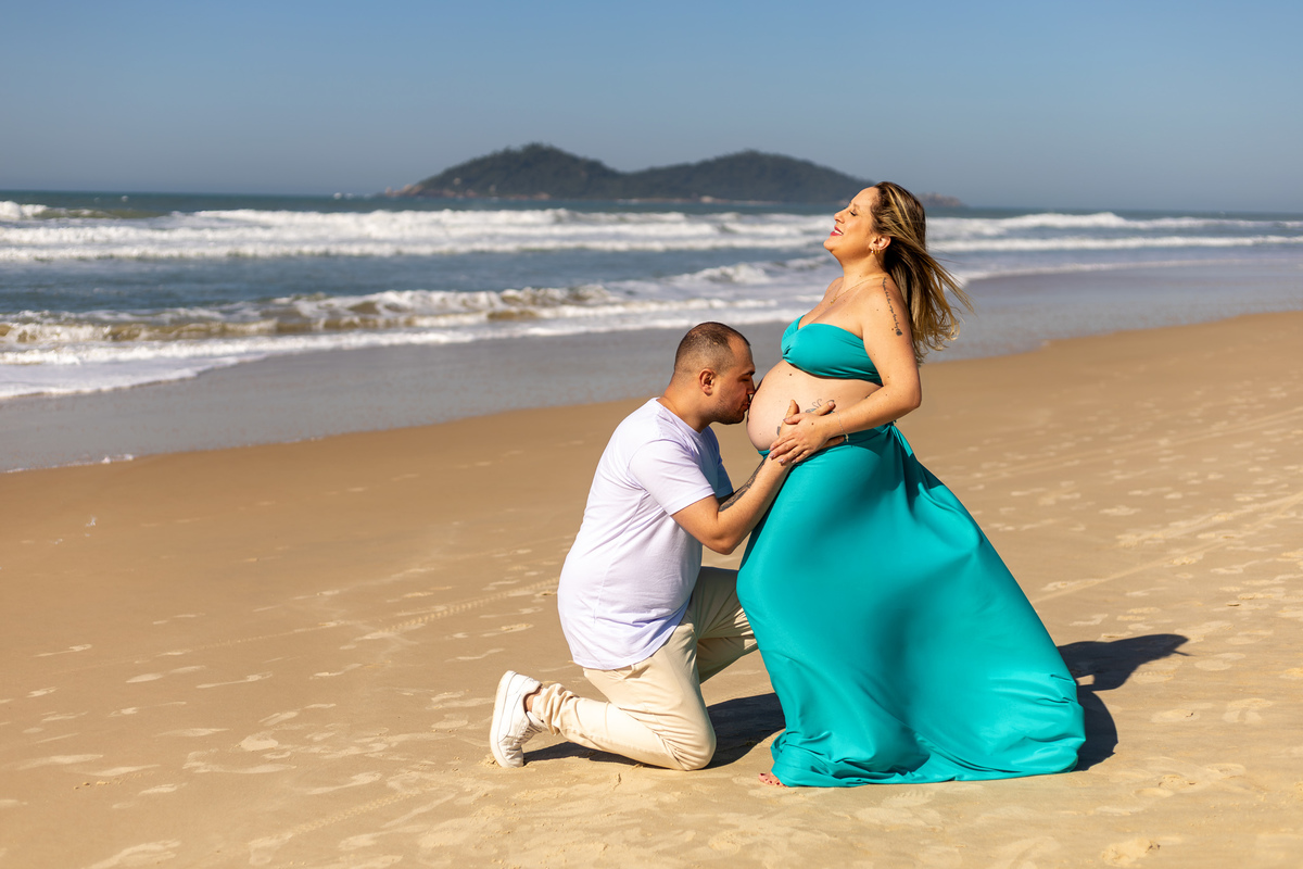 Companheiro beija a barriga da gestante diante do mar no Sul da Ilha.