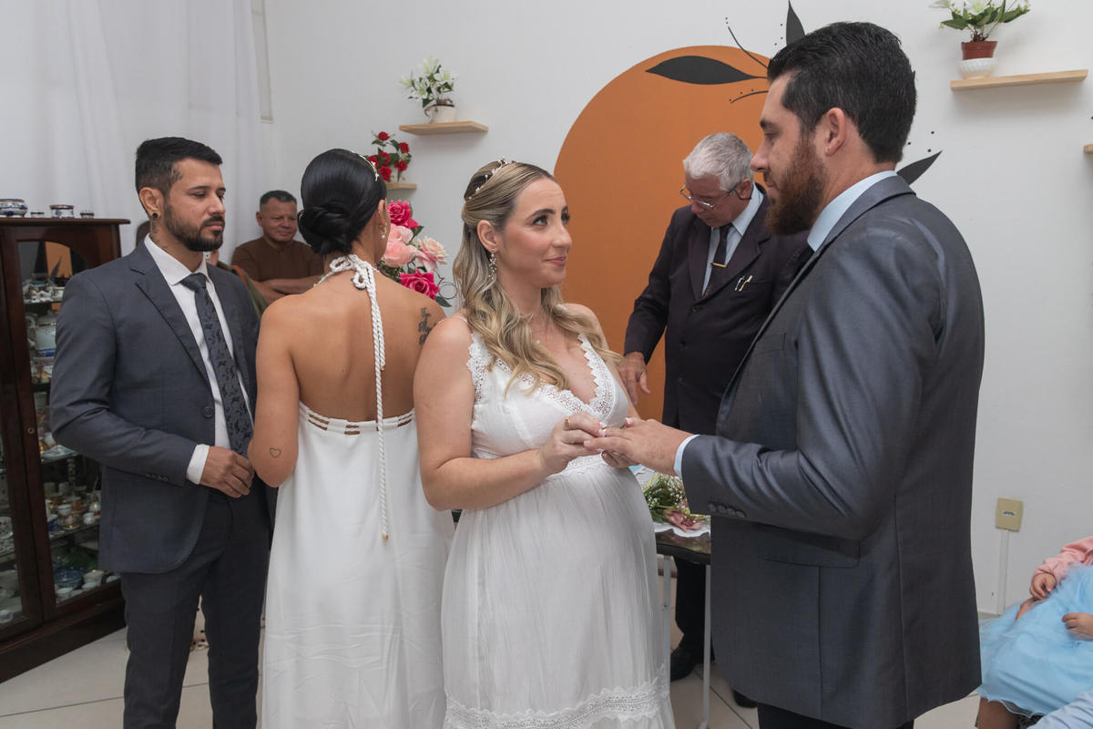 Uma das irmãs realiza a troca de alianças enquanto o segundo casal participa da cerimônia.