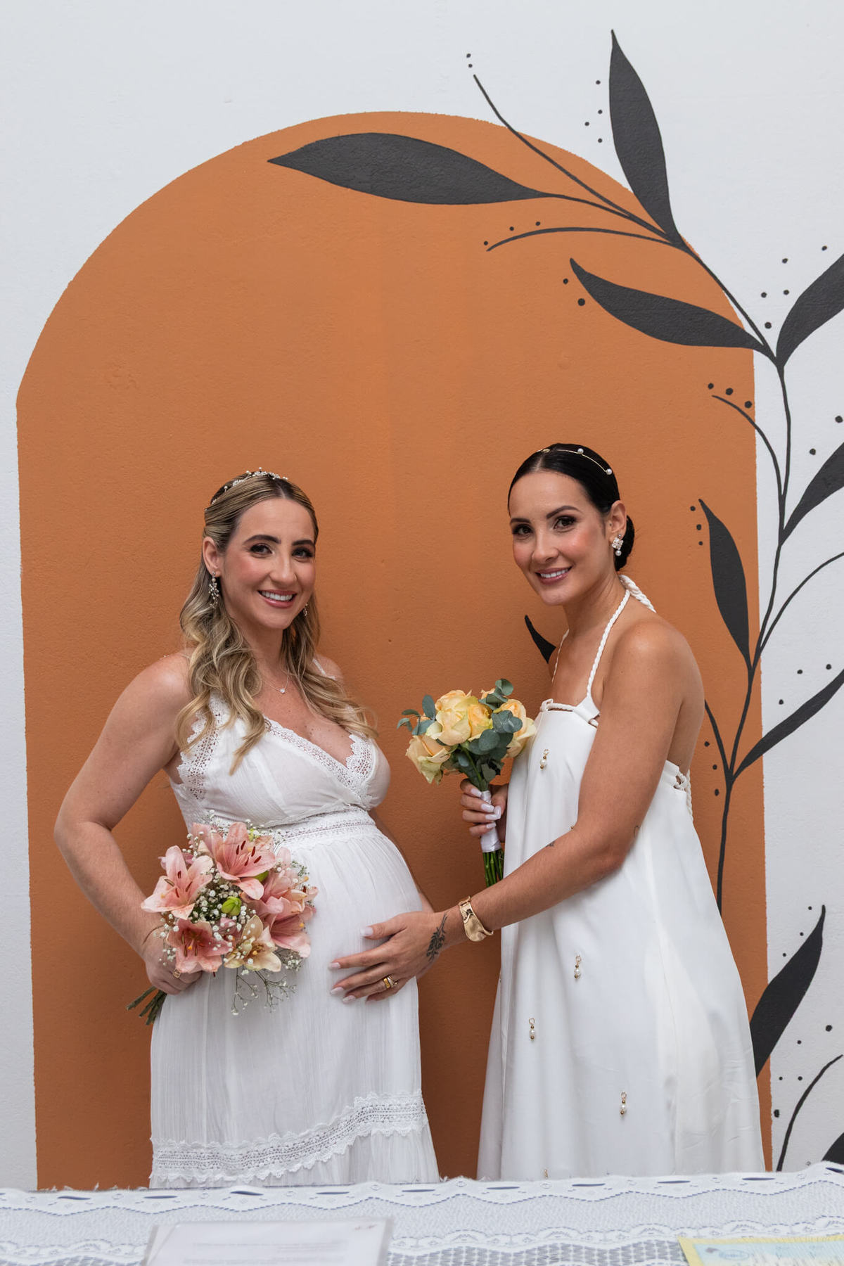 Retrato das irmãs Tais e Talissa vestidas de noiva e segurando seus buquês.