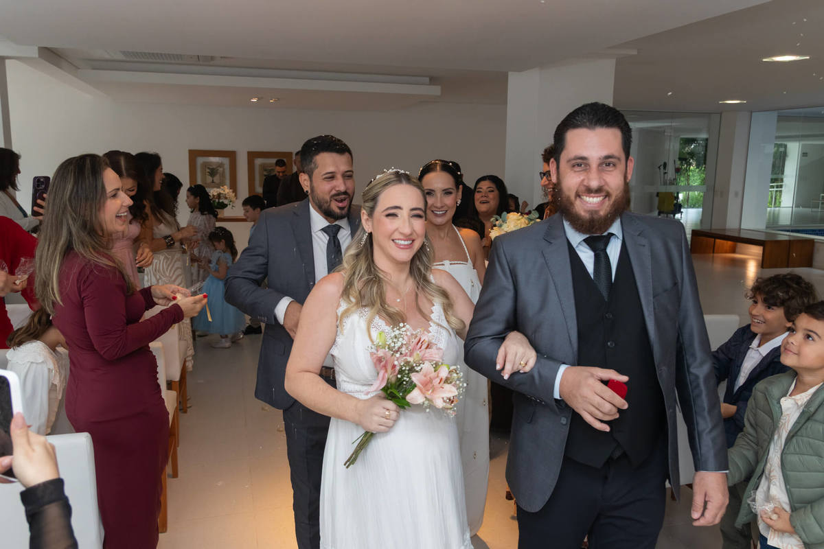 Recém-casados celebram a saída da cerimônia entre sorrisos e convidados.