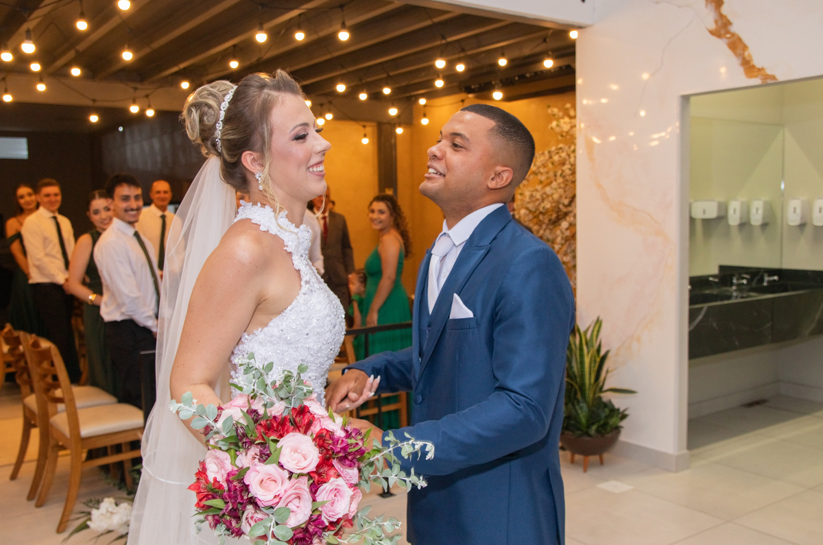 Ana e Vitor sorrindo após a cerimônia, com o buquê da noiva em destaque.