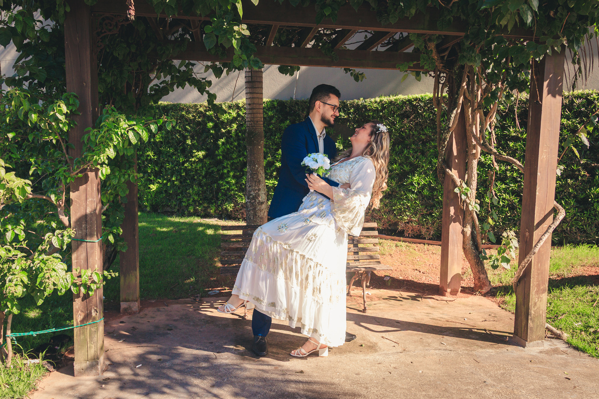 Casal se beijando sob um pergolado de madeira durante o ensaio externo após o casamento civil.