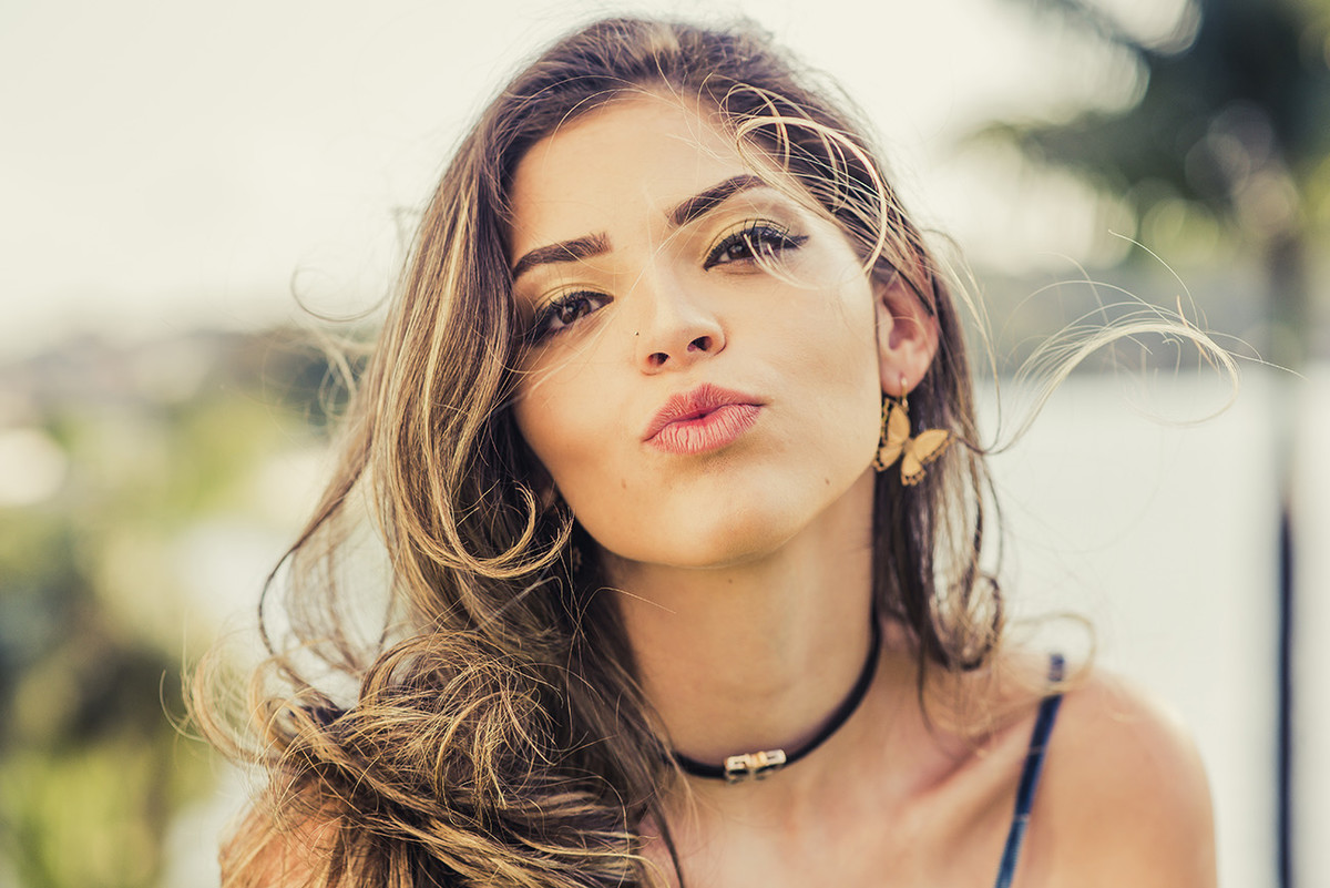 Debutante mandando beijo com cabelos ao vendo com uma bela vista de fundo da lagoa da Pampulha no ensaio de debutante em Belo Horizonte BH MG